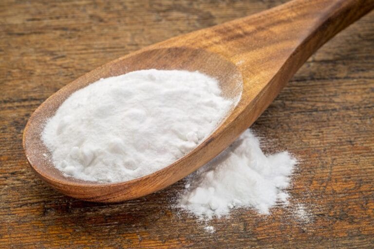 Farine blanche dans une cuillère en bois sur une surface en bois naturel.